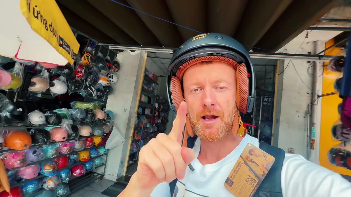 Marcin mit neuem Helm vor einem Helmladen in Da Nang, hinter ihm Regale voller Helme