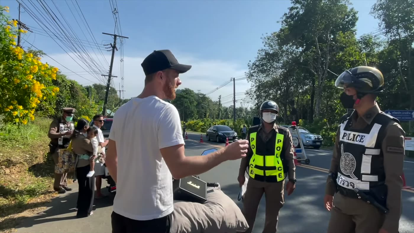 Marcin schiebt seinen Roller an einer Polizeikontrolle in Phuket vorbei und grüßt die Beamten